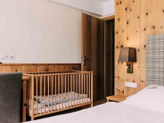 Kinderfreundliches Hotelzimmer mit Gitterbett und alpinem Design